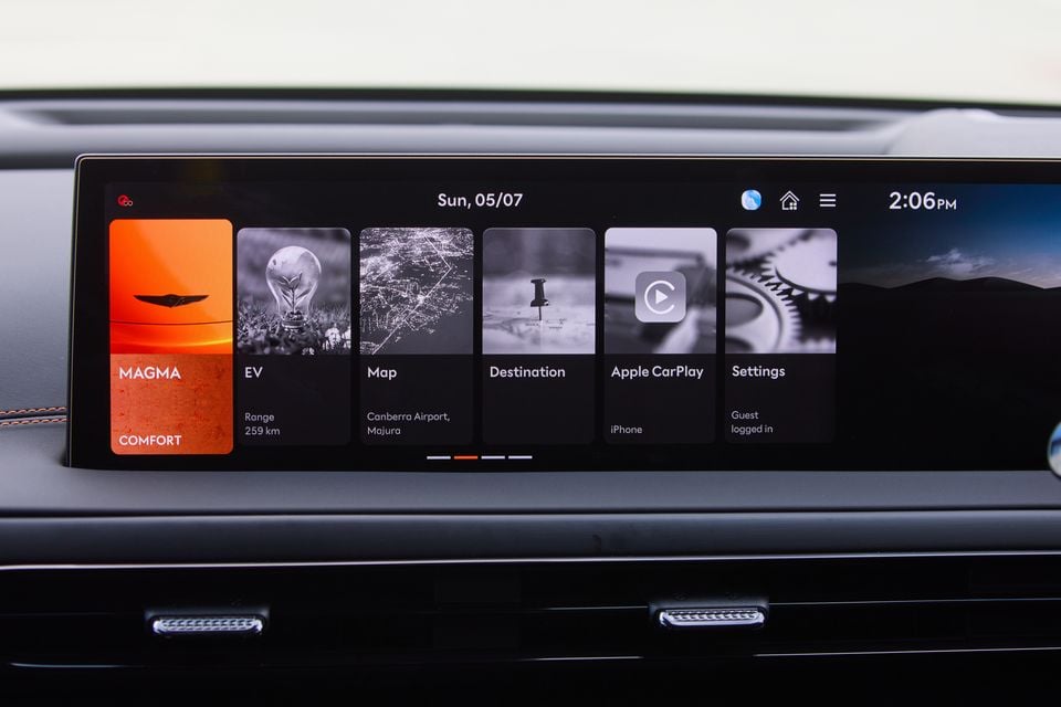 The infotainment touchscreen of a Genesis GV60 Magma showing the home screen with EV range, map, destination, Apple CarPlay and settings tiles