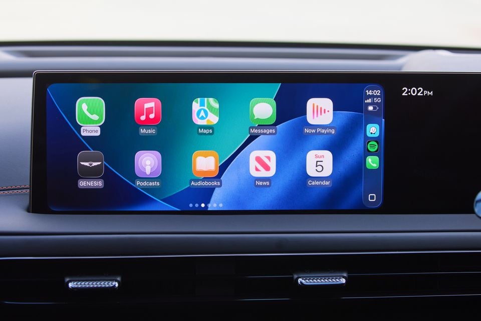 Apple CarPlay interface displayed on the widescreen infotainment touchscreen of a Genesis GV60, showing apps including Phone, Music, Maps, Messages, Podcasts, and Calendar