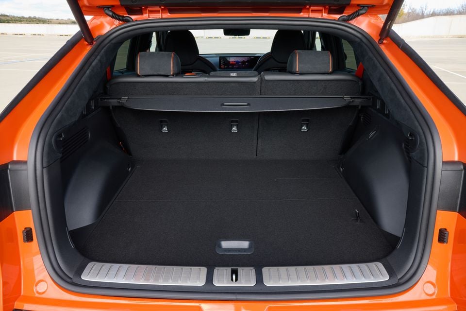 Open boot of an orange 2026 Genesis GV60 Magma showing a spacious, empty cargo area with a retractable cargo blind and three ISOFIX anchor points