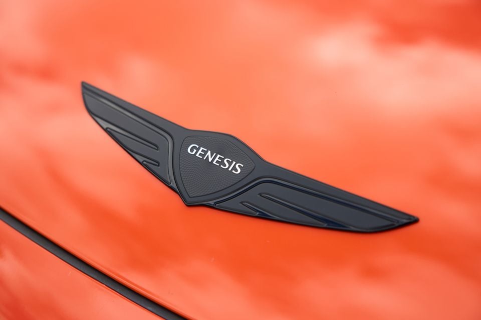Close-up of the Genesis winged badge on an orange Genesis GV60 Magma