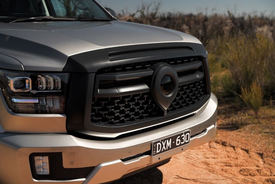 Close-up of the grille and headlight on a silver 2026 GWM Cannon Alpha ute, parked on a dirt track.