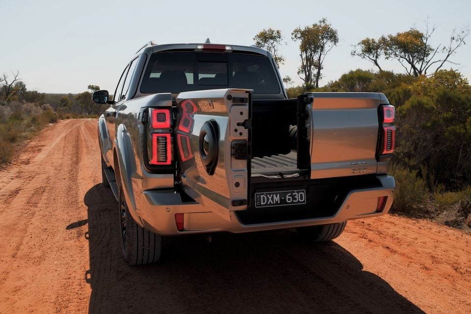 A silver 2026 GWM Cannon Alpha 4x4 dual-cab ute with its tailgate open, parked on a red dirt road, seen from the rear