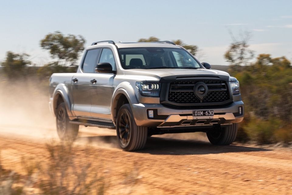 A silver 2026 GWM Cannon Alpha ute kicks up dust while driving on a dirt road, seen from the front quarter.