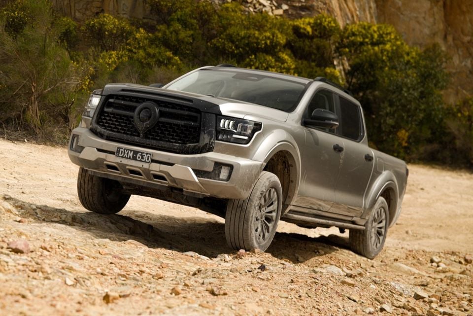 A silver 2026 GWM Cannon Alpha dual-cab ute driving on a rocky dirt trail, seen from the front quarter.
