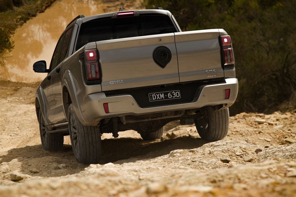 A silver 2026 GWM Cannon Alpha dual-cab ute driving away from the camera on a muddy off-road track