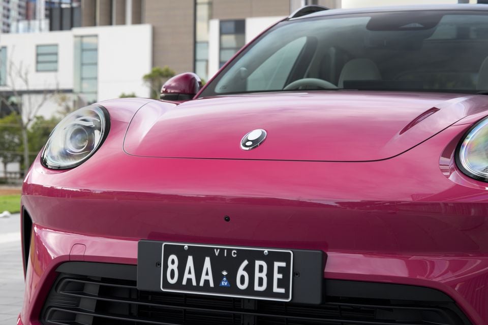 Close-up of the front of a pink 2026 GWM ORA 5 SUV with a Victorian EV licence plate, showing the bonnet badge and headlights
