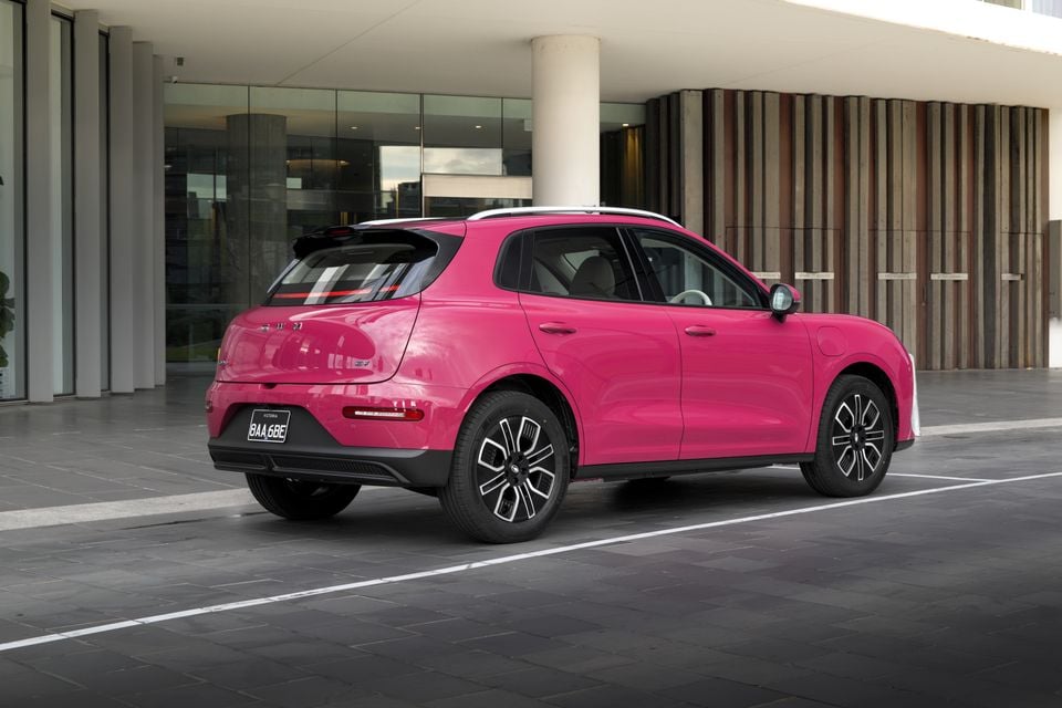 A pink 2026 GWM ORA 5 SUV seen from the rear three-quarter angle, parked outside a modern building