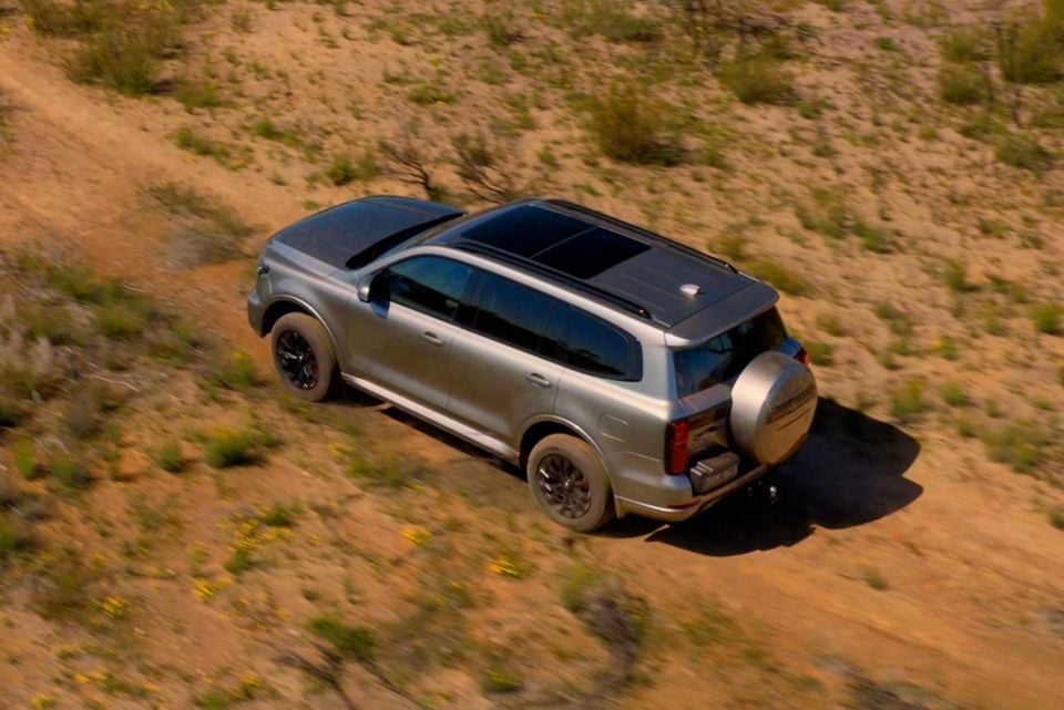 A silver 2026 GWM Tank 500 SUV with a rear-mounted spare wheel drives along a dirt trail, seen from above.