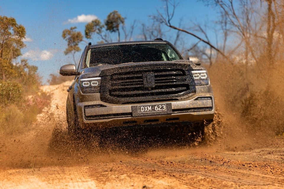 A grey 2026 GWM Tank 500 SUV driving through mud and dirt on an off-road track, seen from the front