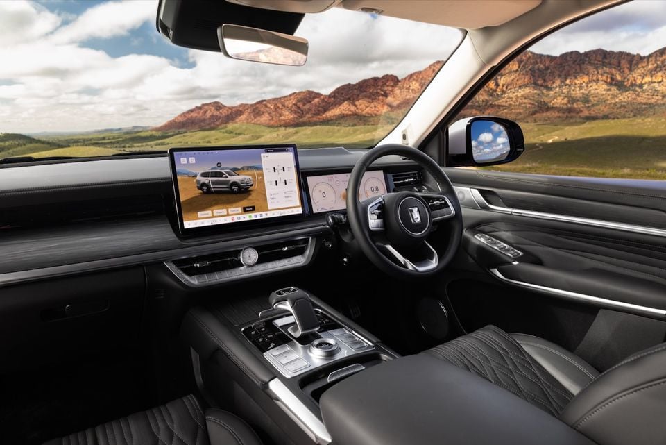 The black leather interior of a 2026 GWM Tank 500 showing the dashboard, steering wheel and dual digital screens, with mountains visible through the windscreen