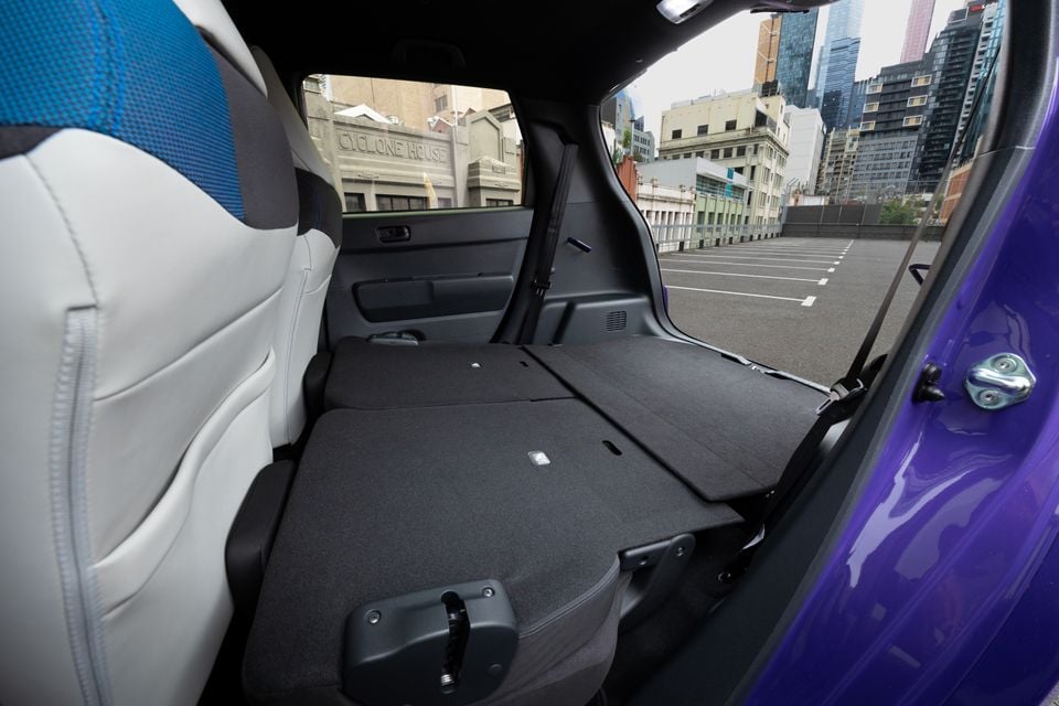 Inside a purple Honda Super One, the rear seats are folded flat to expand cargo space, with a city car park visible through the tailgate.