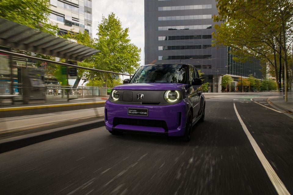 A purple 2026 Honda Super-ONE electric hatchback driving through a city street, seen from the front.