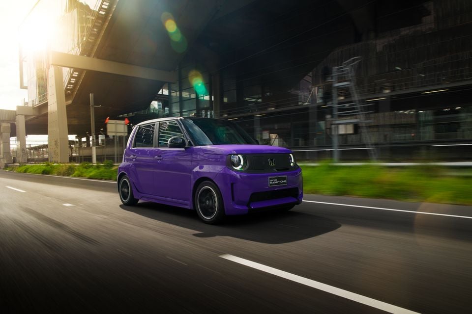 A purple 2026 Honda Super-ONE compact electric hatchback driving on a city road beneath an elevated railway.