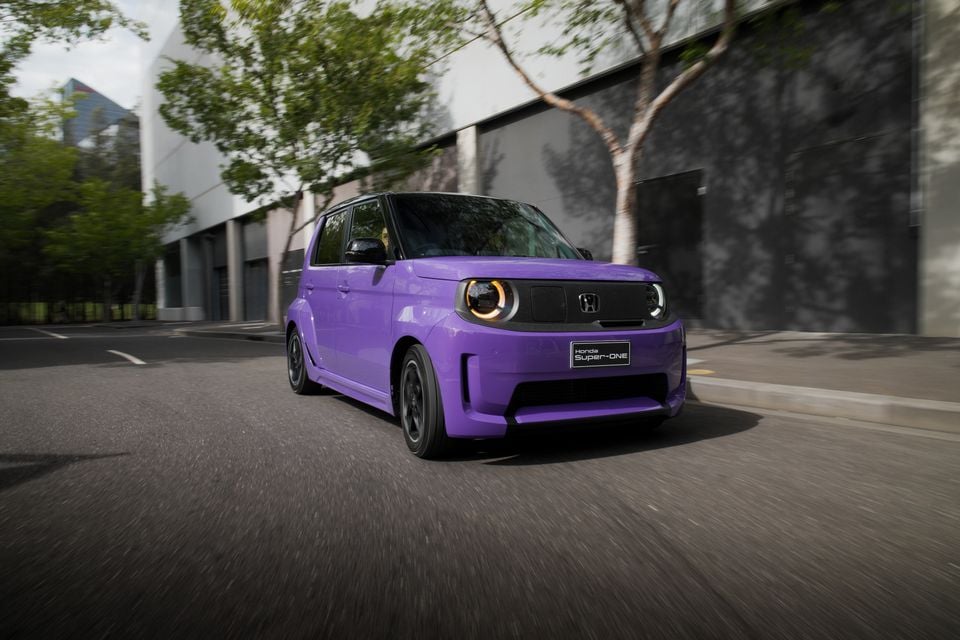A purple 2026 Honda Super-One compact hatchback driving through a city street, seen from the front quarter angle.