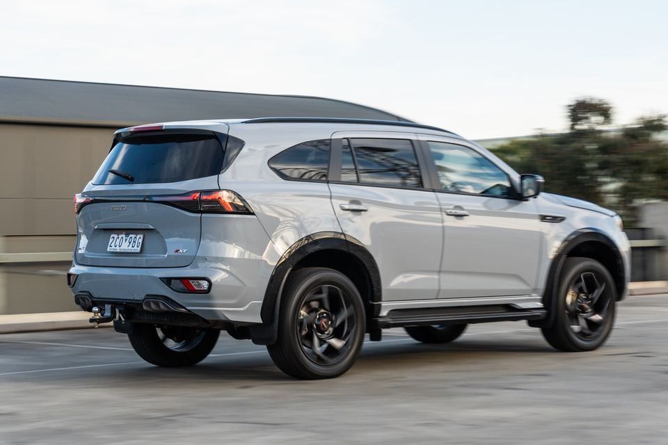 A silver 2026 Isuzu MU-X X-Terrain SUV seen from the rear three-quarter angle, driving in an urban area
