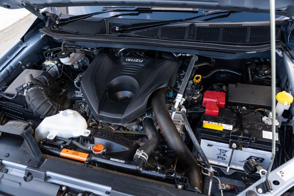 The engine bay of a 2026 Isuzu MU-X, showing the Isuzu-branded engine cover, battery, and supporting components with the bonnet open.