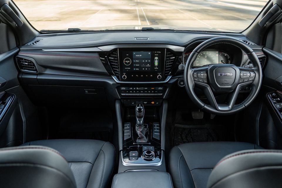 Interior of the 2026 Isuzu MU-X X-Terrain showing the dashboard, central touchscreen infotainment system, dual-zone climate controls, gear shifter, and Isuzu-branded steering wheel with right-hand drive layout