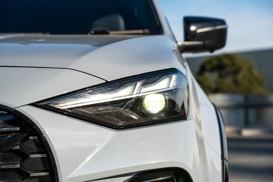 Close-up of the headlight on a white Isuzu MU-X X-Terrain, with the light illuminated