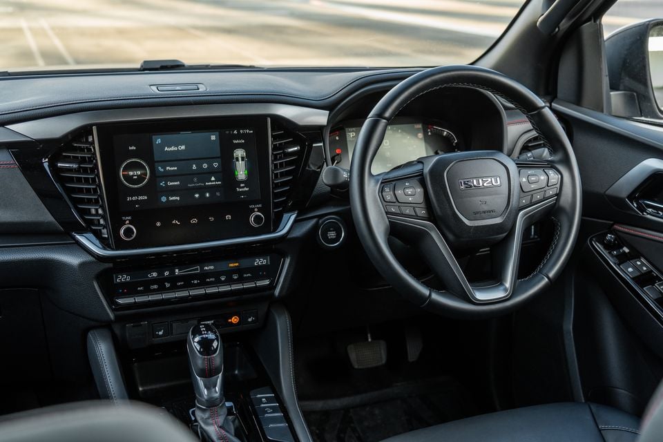Interior of a 2026 Isuzu MU-X X-Terrain showing the dashboard, Isuzu steering wheel, touchscreen infotainment system with Apple CarPlay and Android Auto, dual-zone climate controls, and gear shifter