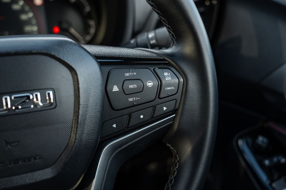 Close-up of the Isuzu MU-X steering wheel showing cruise control and driver assist buttons including SET/+, SET/-, RES, MODE and CANCEL