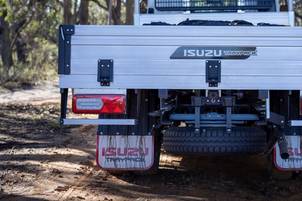 The rear tray and badge of a 2026 Isuzu NMS 45-150 AWD truck parked on a dirt track in the bush