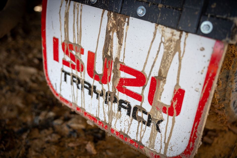 A mud-splattered mud flap on an Isuzu truck shows the Isuzu logo and "Traypack" text.
