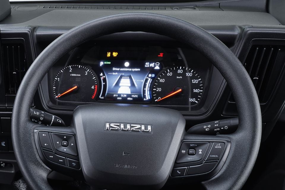 Close-up of an Isuzu truck's steering wheel and instrument cluster, showing the driver assistance display and badge