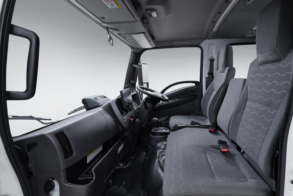 The cabin of a 2026 Isuzu NMS 45-150 AWD truck showing a wide bench seat and dashboard with a small infotainment screen.