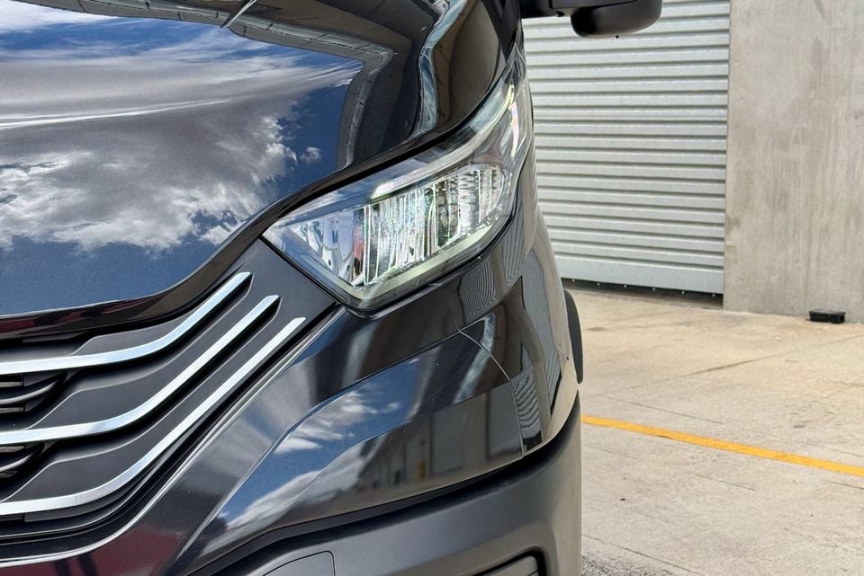 Close-up of the front corner of a dark grey van showing the headlight and chrome grille detail