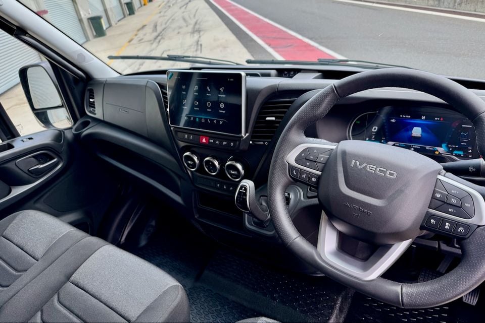 Interior of an Iveco Daily van showing the steering wheel, large central touchscreen infotainment system, digital instrument cluster, and dashboard controls from the driver's seat