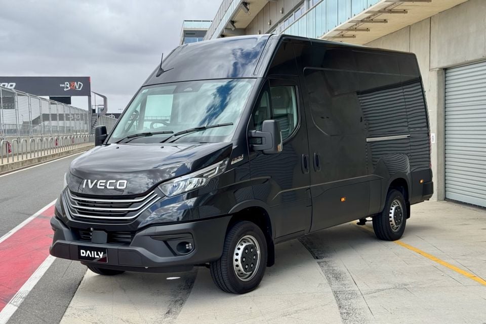 A black Iveco Daily van seen from the front-side angle, parked at a motorsport circuit pitlane area