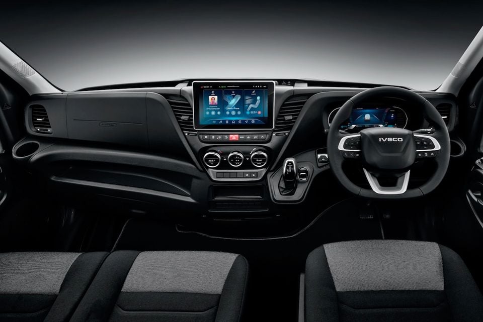 Interior of an Iveco Daily van showing the dashboard, large central touchscreen infotainment display, Iveco-branded steering wheel, digital instrument cluster, and climate controls, with front seats visible in the foreground.