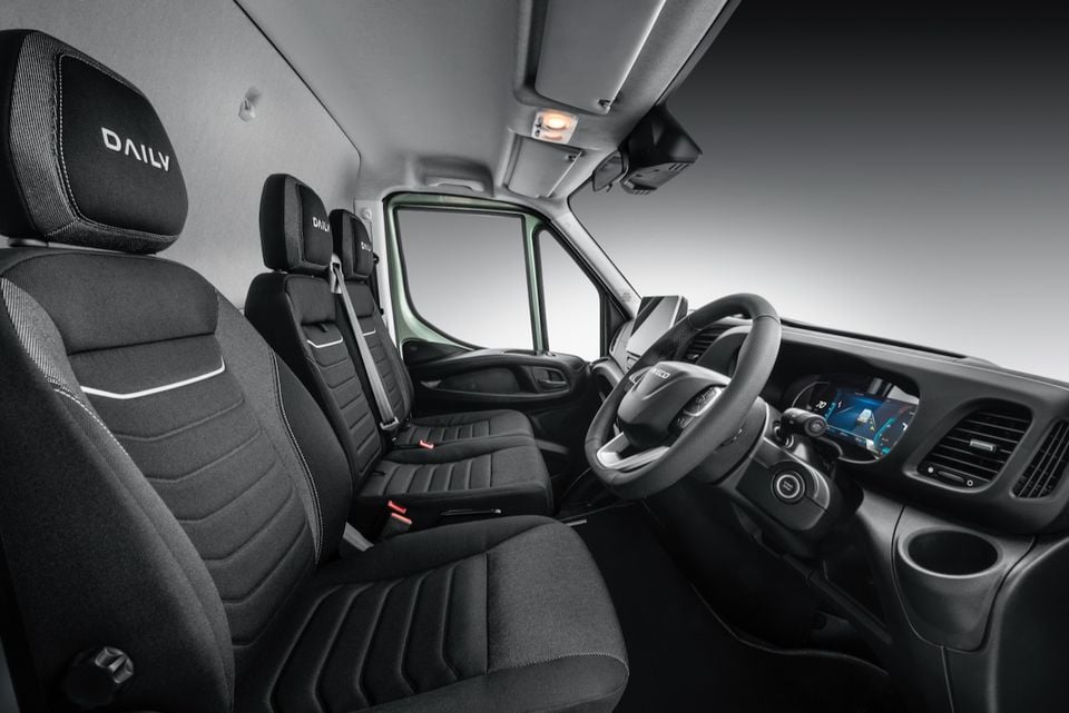 Interior of the Iveco Daily van showing the front cabin with black fabric seats branded with the Daily logo, steering wheel, digital instrument cluster, and infotainment touchscreen