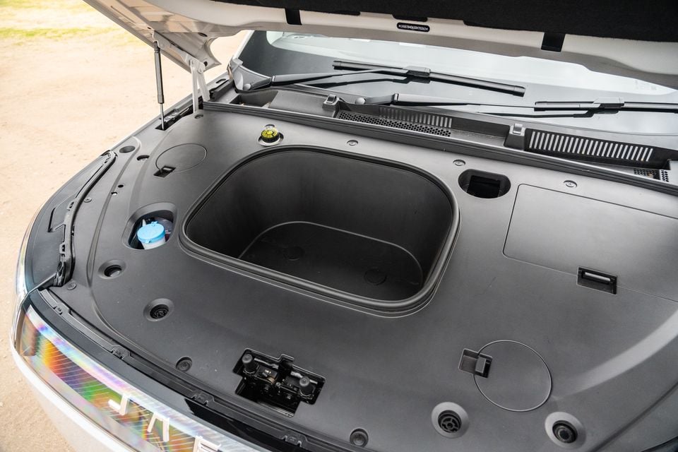 The front storage compartment (frunk) of a 2026 Jaecoo J5 EV open and empty, showing a large storage bin and washer fluid reservoir