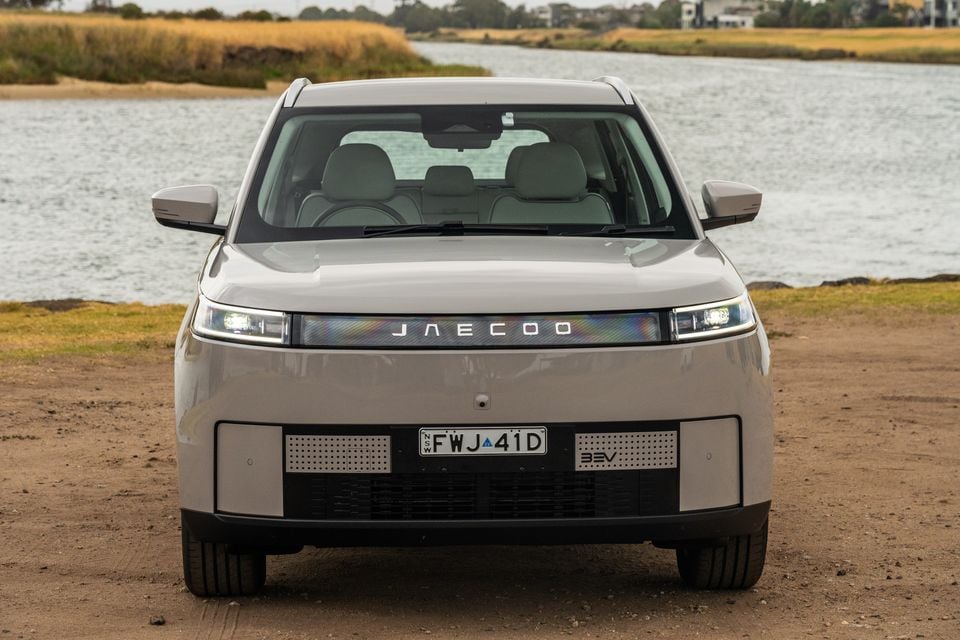 A Jaecoo J5 EV SUV seen from the front, parked on a dirt surface beside a waterway