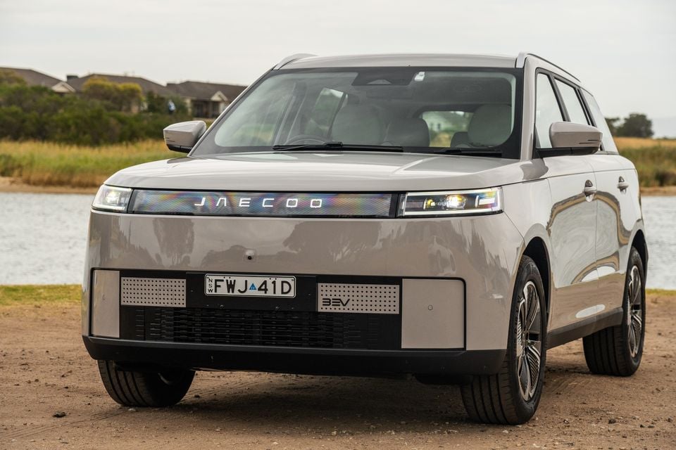 A Jaecoo J5 EV SUV seen from the front, parked on a dirt surface near water