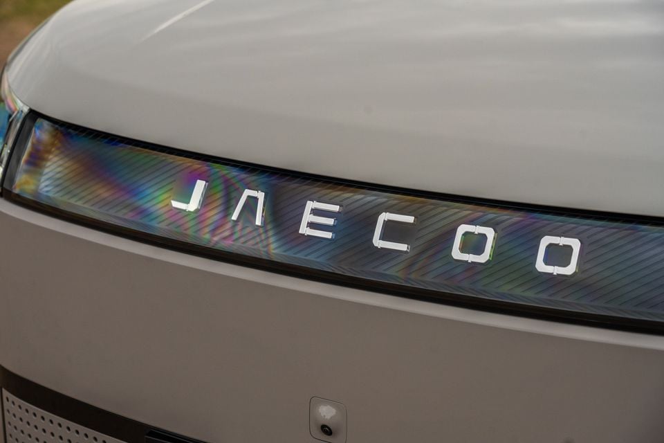 Close-up of the Jaecoo J5 EV's front fascia showing the illuminated 'Jaecoo' lettering across an iridescent light bar