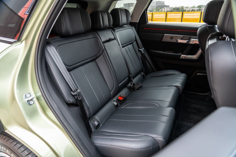 The rear seat interior of a 2026 Jaecoo J7, showing black leather bench seating with white contrast stitching, seatbelts, and door trim detail in an SUV with a green exterior