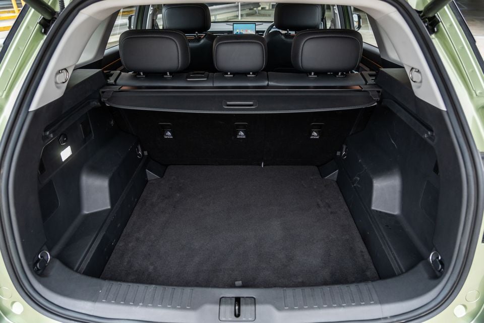 The empty boot of a green 2026 Jaecoo J7 SUV, viewed from the rear with the tailgate open, showing a carpeted load floor and retractable cargo cover