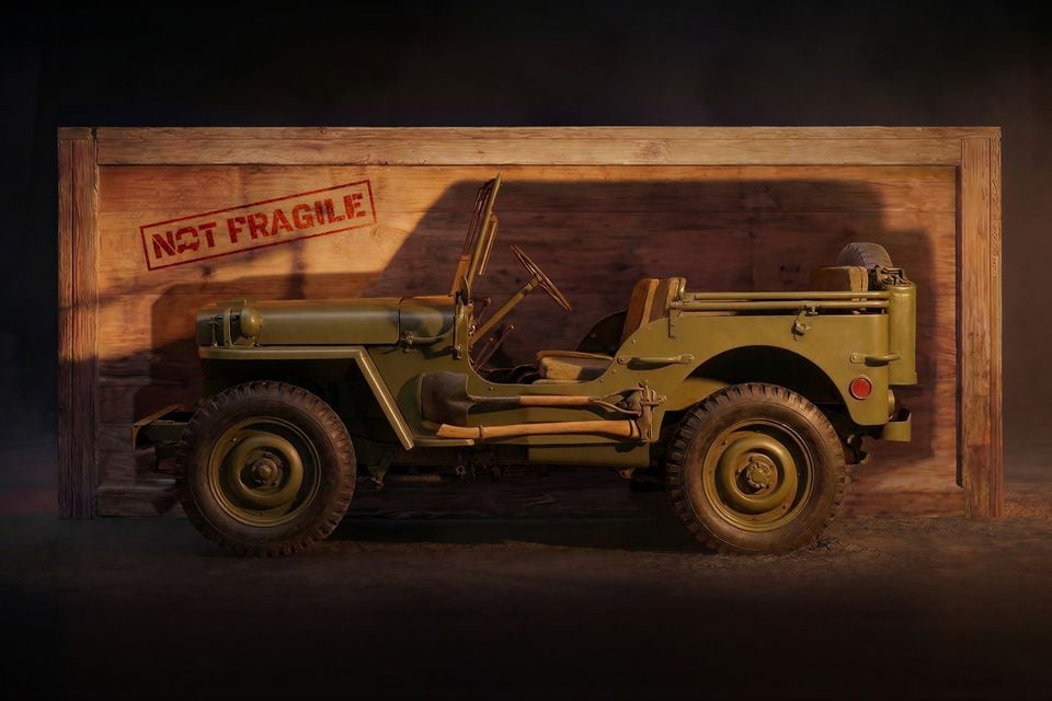 An olive green classic Willys military Jeep seen side-on in front of a wooden crate stamped 'Not Fragile', in a Jeep teaser image