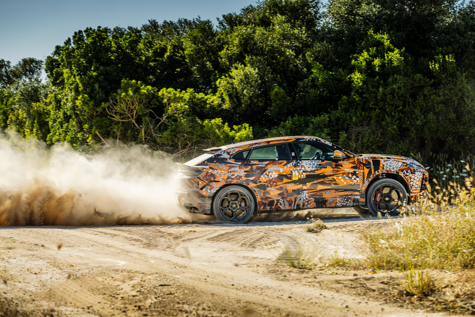 A camouflaged Lamborghini Urus Performante prototype kicking up dust on a dirt track, seen from the side