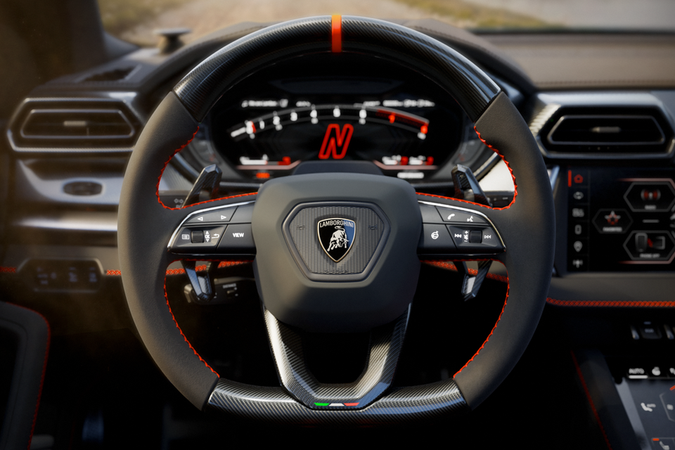 Lamborghini Urus Performante steering wheel with carbon fibre accents, red stitching, and Italian flag detail, with the digital instrument cluster visible behind
