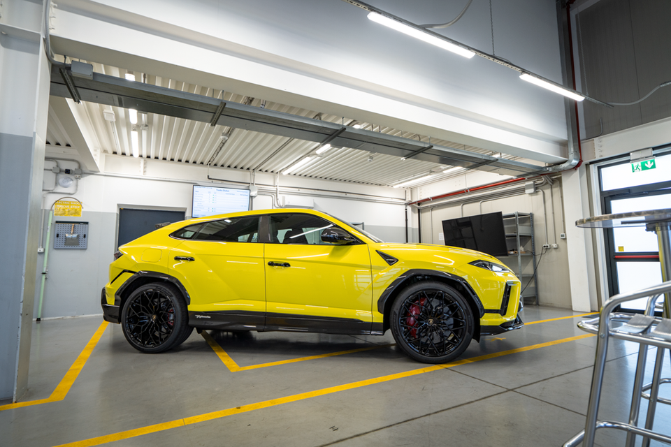 A yellow Lamborghini Urus Performante SUV seen from the side, parked inside a facility with black alloy wheels and carbon fibre trim details.