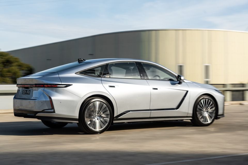 A silver 2026 Lexus ES 350e sedan seen from the rear three-quarter angle while driving on a road