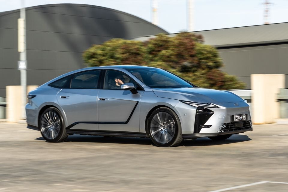 A silver 2026 Lexus ES 350e Sports Luxury fastback sedan driving through a car park, seen from the front-side
