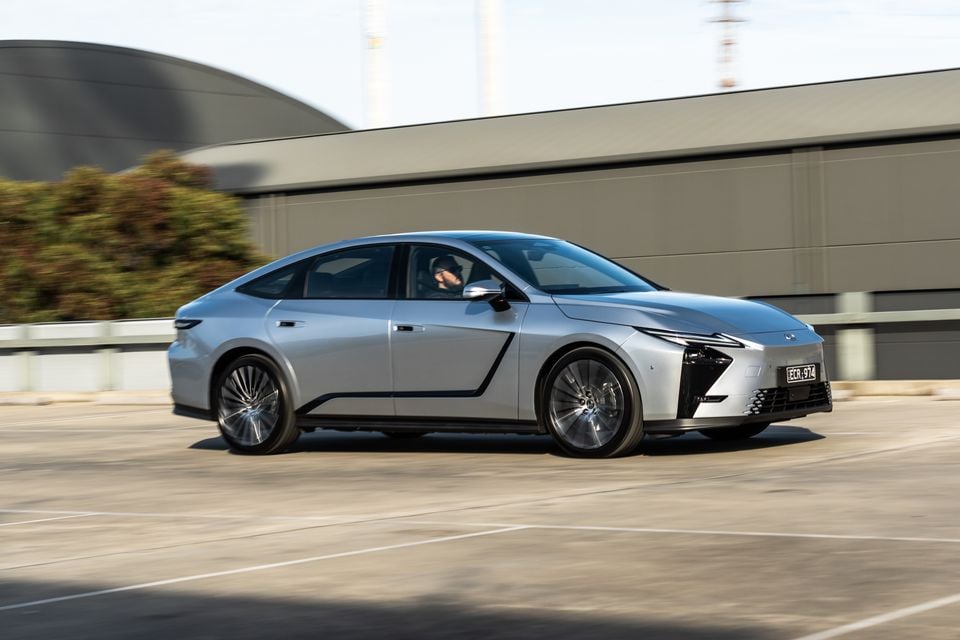 A silver 2026 Lexus ES 350e fastback sedan seen from the front-side while driving through an urban area