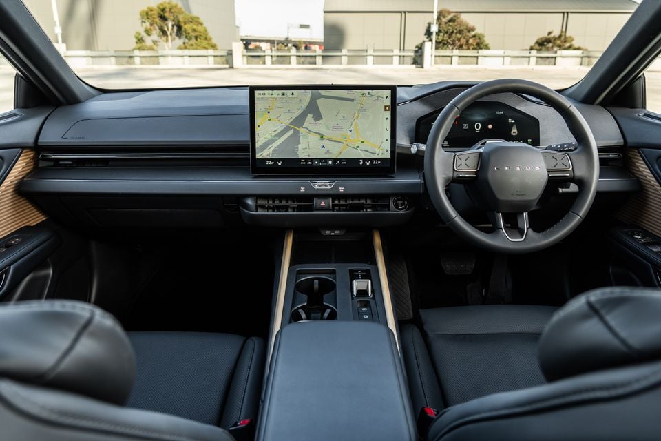 Interior of a 2026 Lexus ES350e showing the dashboard, Lexus-branded steering wheel, central touchscreen displaying navigation, and timber-accented centre console