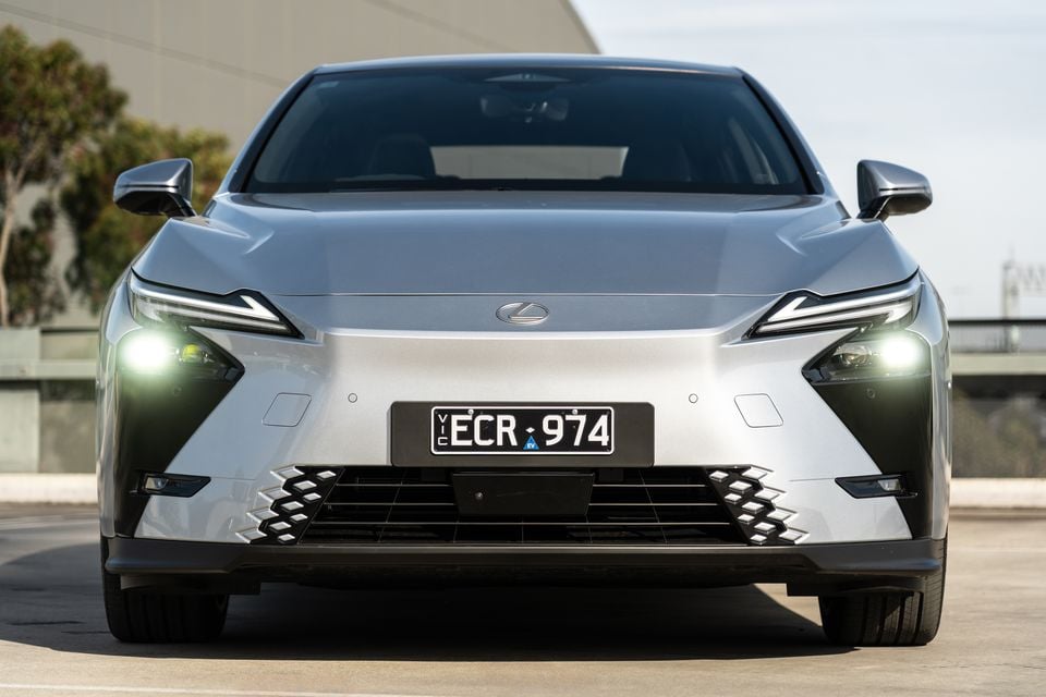 Front view of a silver 2026 Lexus ES 350e with headlights on, seen straight-on in an outdoor carpark with a Victorian EV number plate.