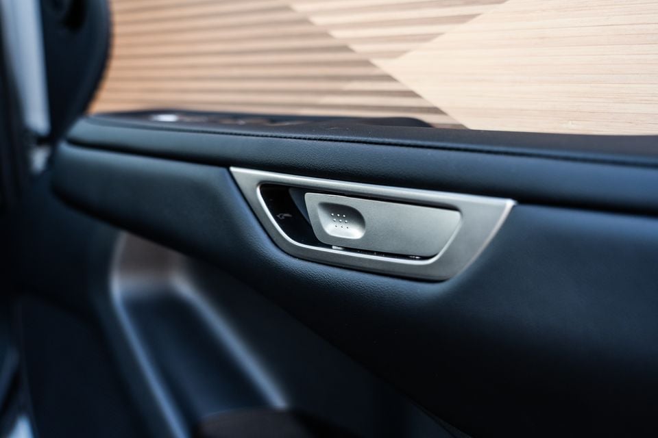 Close-up of the interior door handle and trim panel of a 2026 Lexus ES 350e, showing a brushed silver pull handle set into black leather door lining with wood-look trim above.