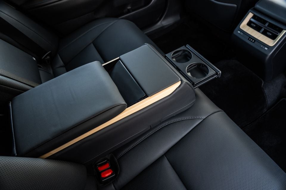 Interior view of the 2026 Lexus ES 350e Sports Luxury showing the centre console armrest with wood trim, storage compartment, and dual cup holders, with rear climate control vents visible in the background